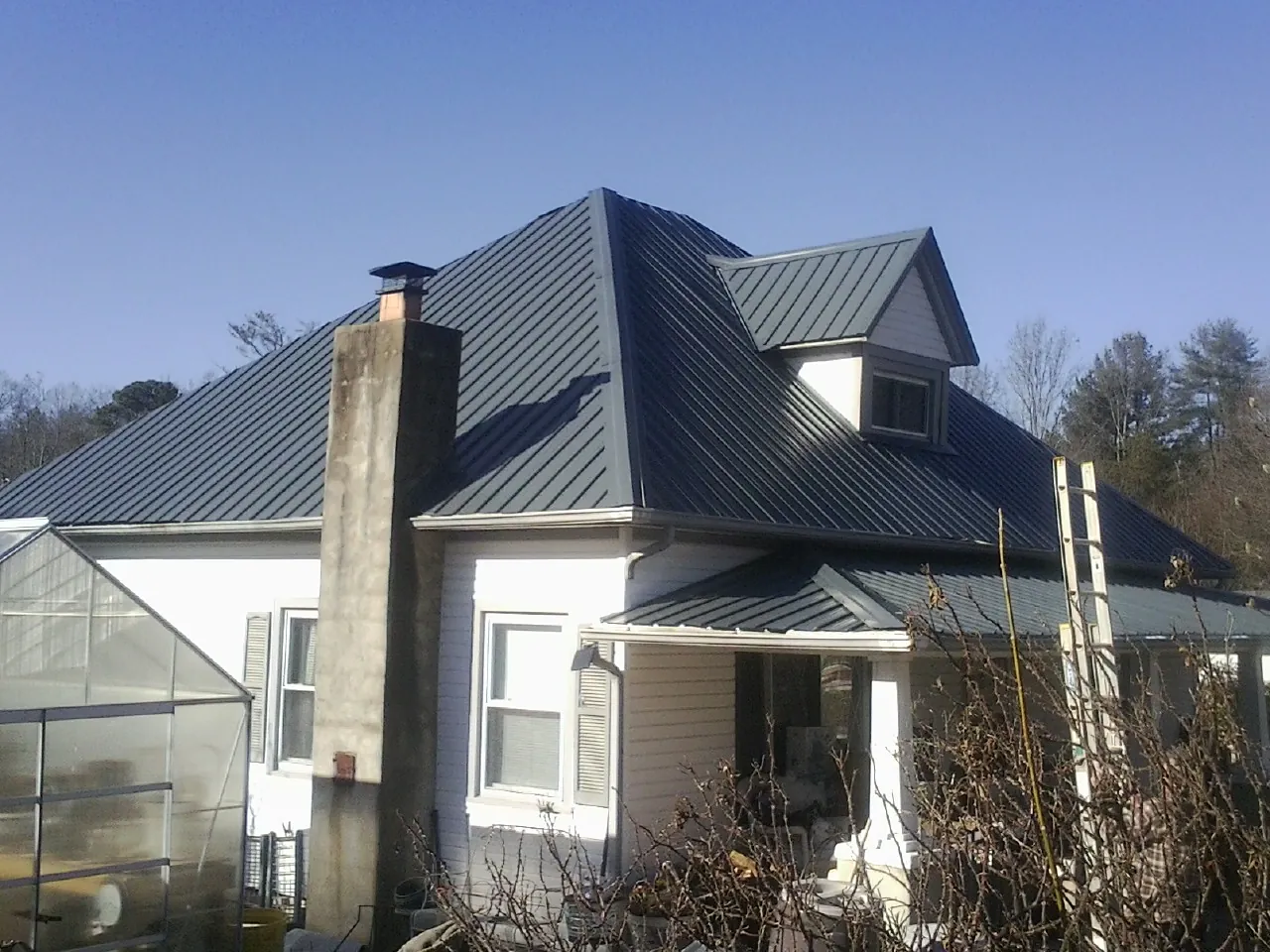 Dark blue standing seam metal roof on a white farmhouse with dormer — Slate & Tile Roof Repair by Roofing Brothers in Louise