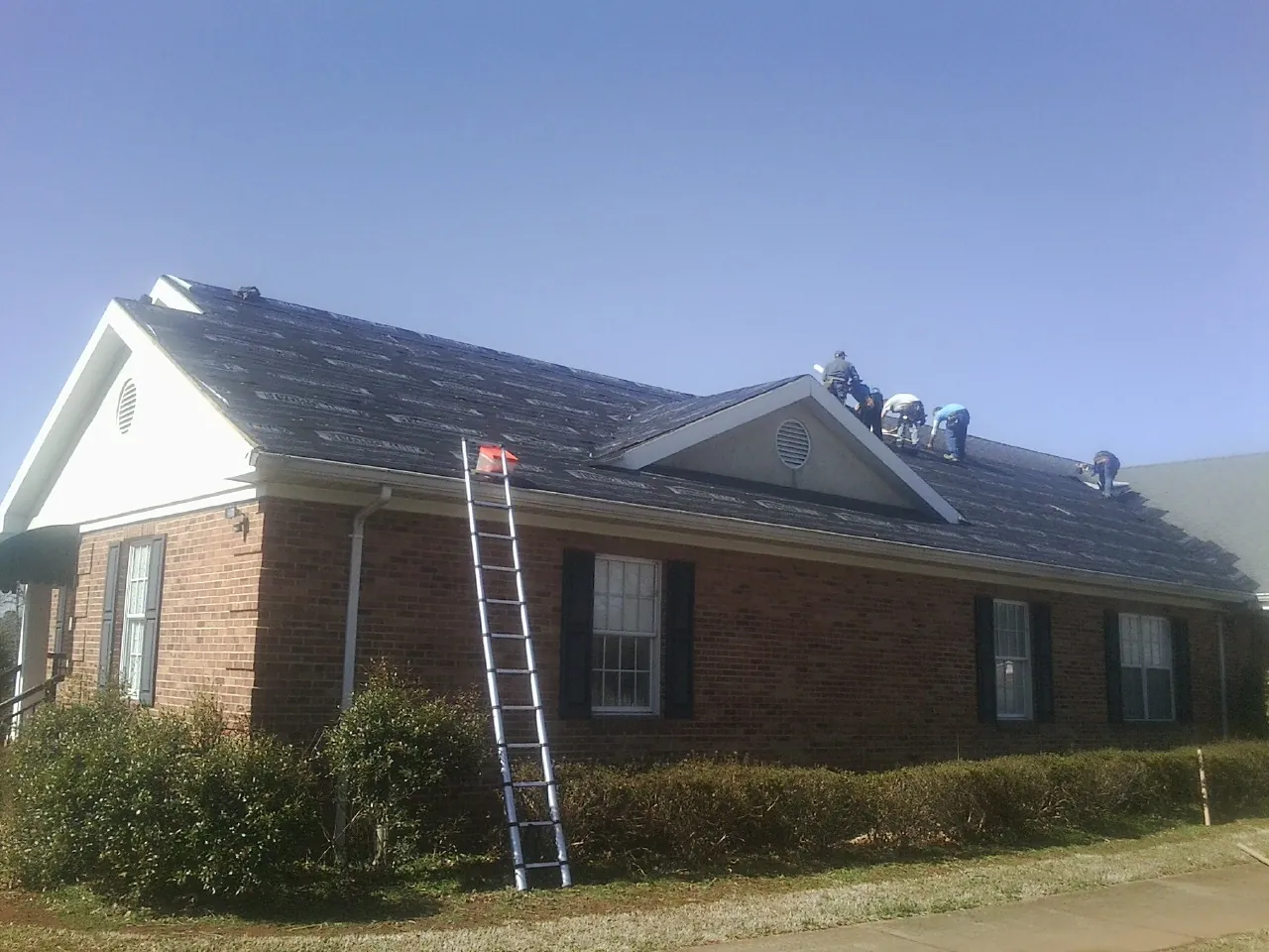 Crew tearing shingles off a brick ranch roof with a ladder set — Metal Roof Repair work by our crew in Louise
