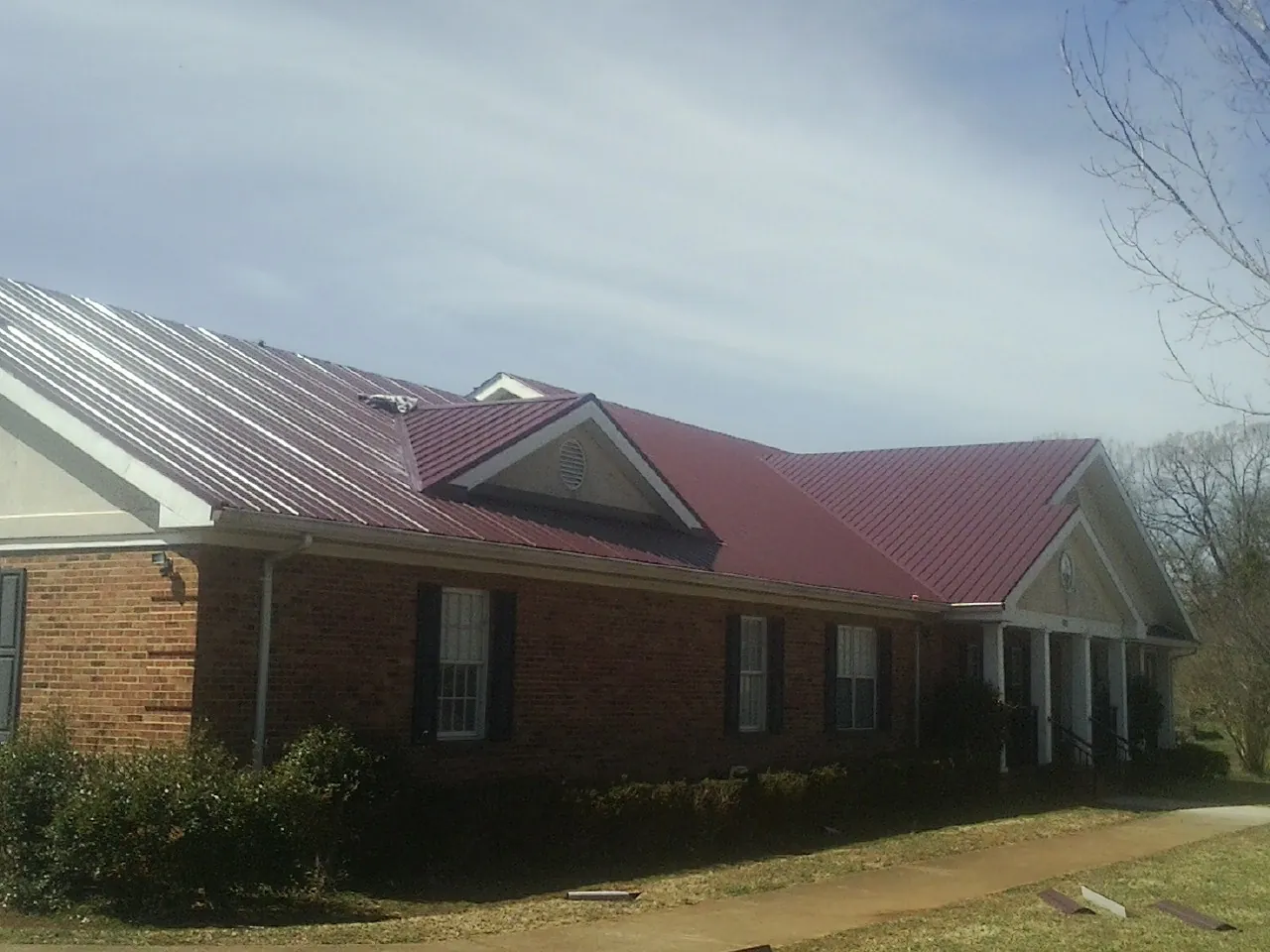 Red metal roof with gabled entries on a long brick building, from a Hail Damage Roof Repair job in Louise