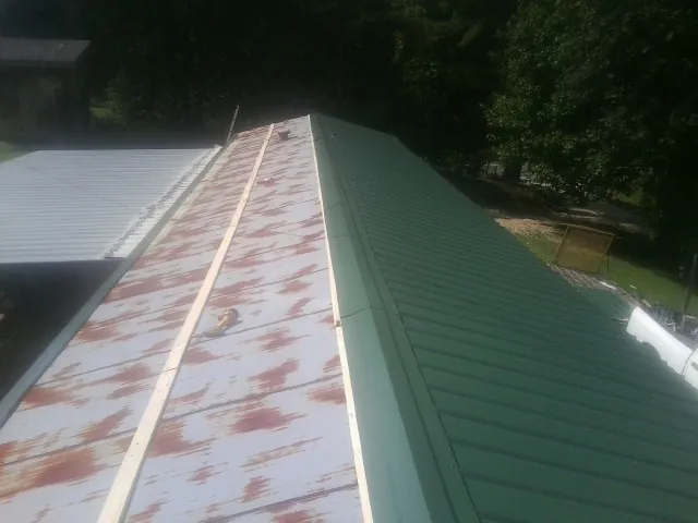 Old rusted panels beside newly installed green metal roofing — Wind Damage Roof Repair by Roofing Brothers in Louise
