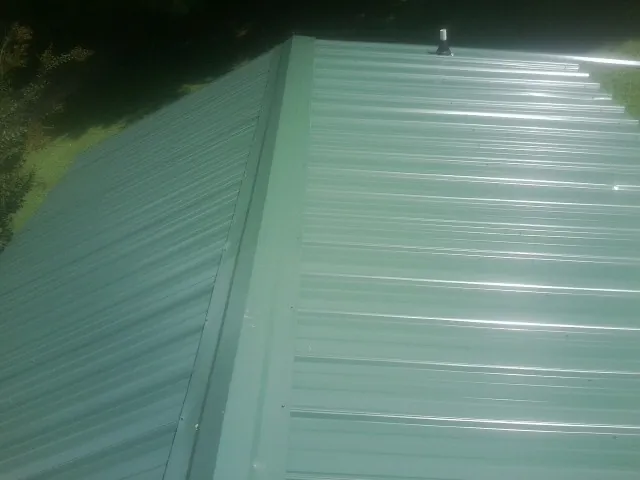 New green metal panels meeting at the ridge of a roof — Flat Roof Repair work by our crew in Louise