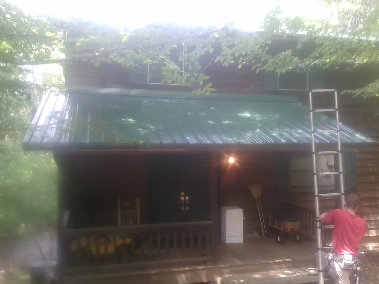 Worker on a ladder at the green porch roof of a wooded cabin in Louise