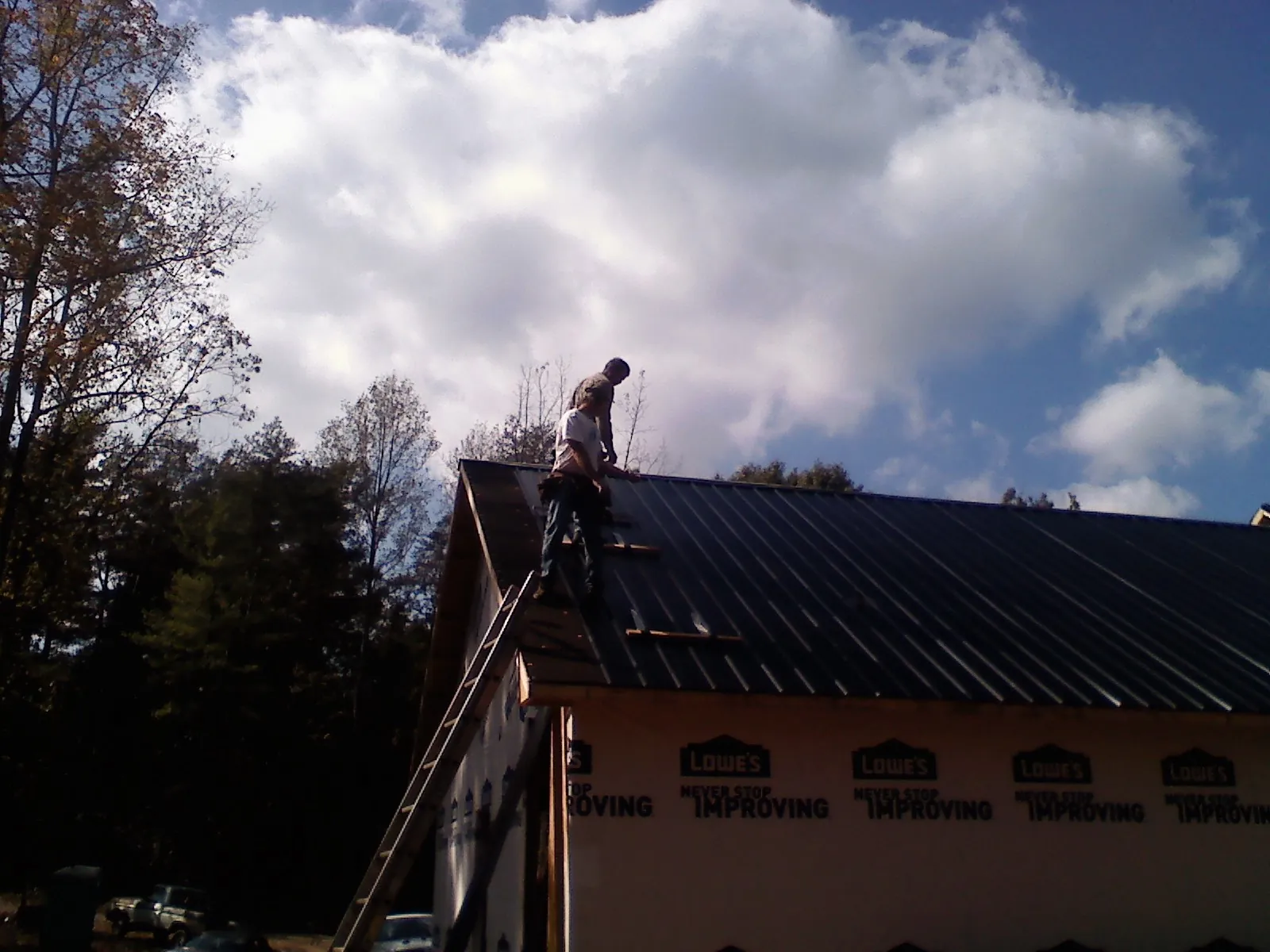 Roofer fastening dark metal panels high against a cloudy sky, from a Roof Inspection job in Louise