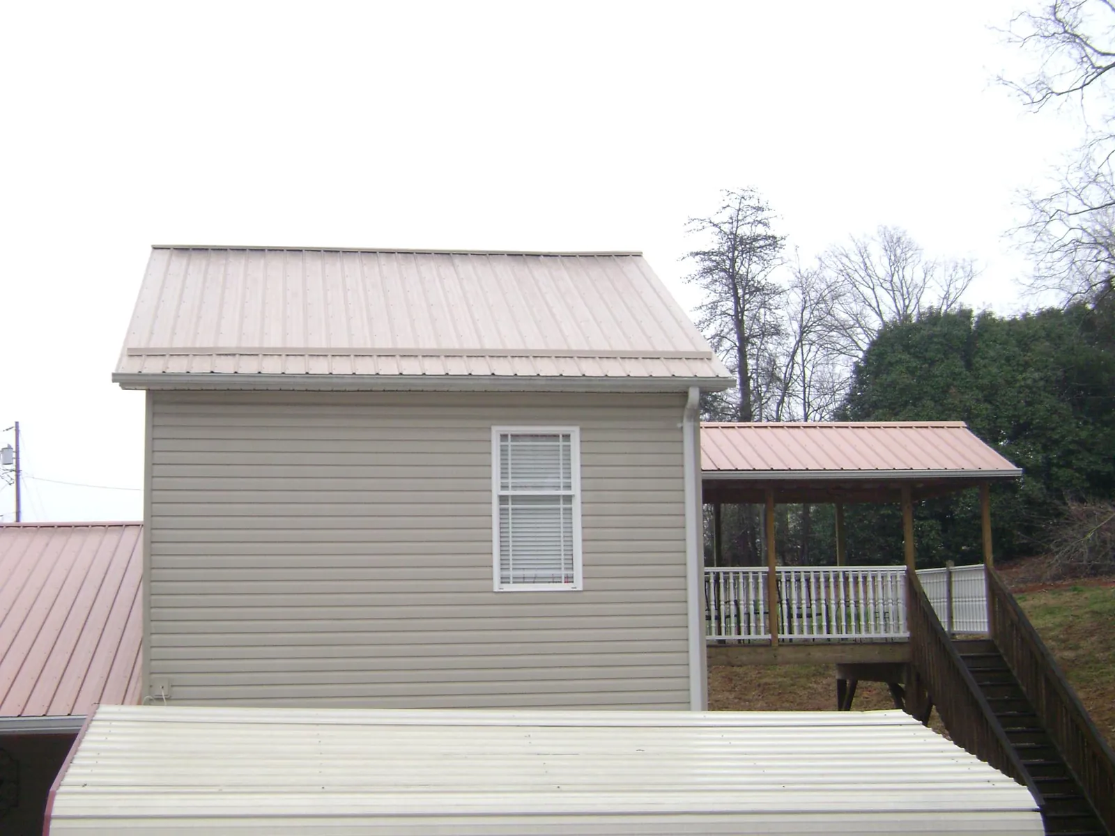Tan metal roofs on a two story addition and attached porch, from a Roof Replacement job in Louise